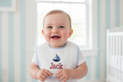 Baby wearing a bib with 'Jack' and a sailboat design, standing in a crib.