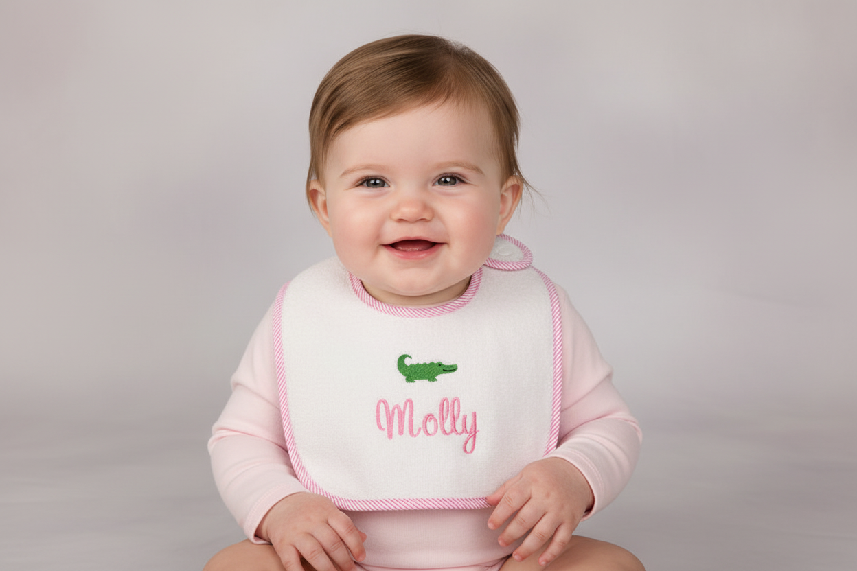 Baby wearing a bib with 'Molly' and a green alligator on a plain background