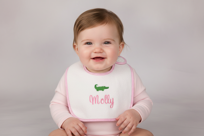 Baby wearing a bib with 'Molly' and a green alligator on a plain background